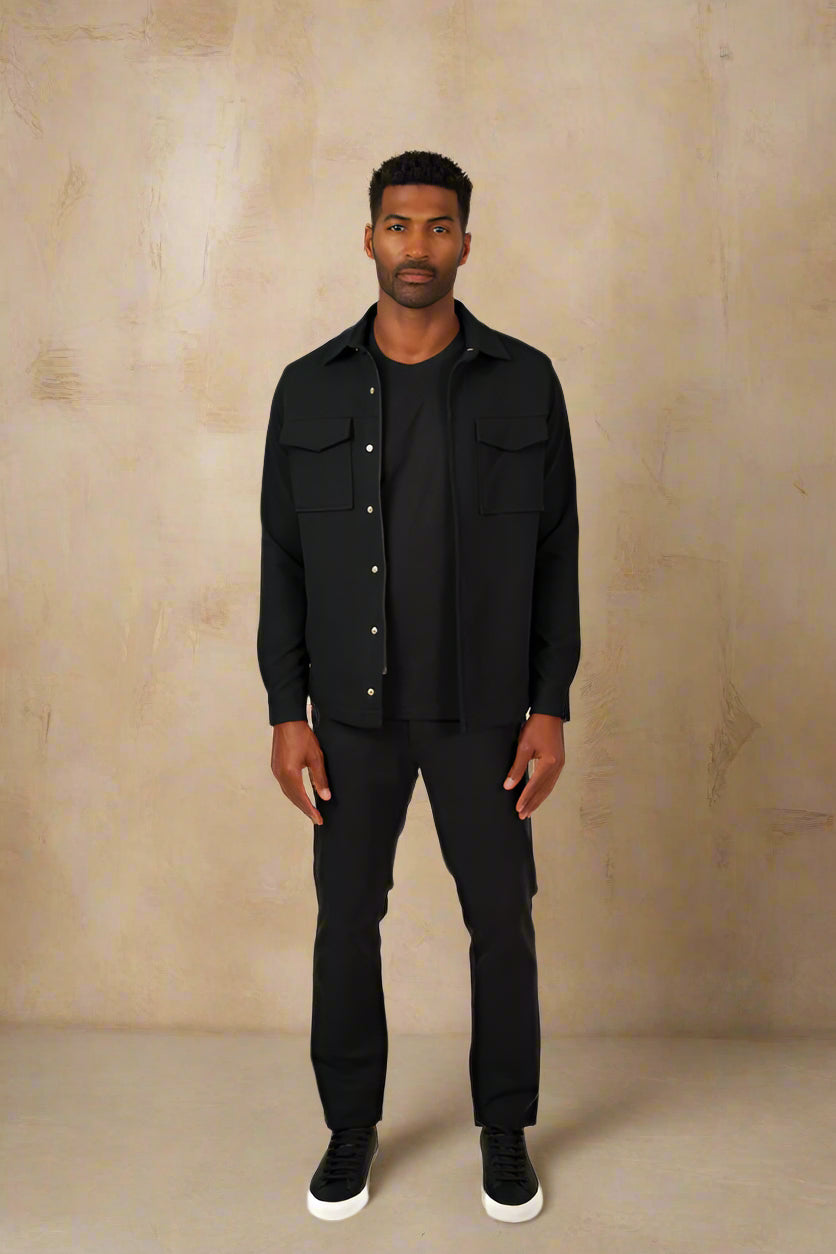 Man wearing a black shirt and pants against a beige wall