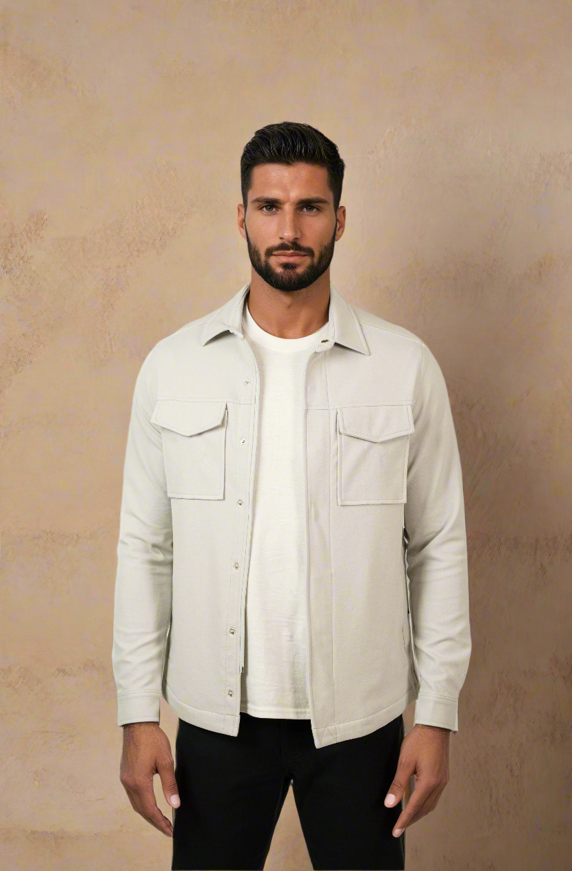 Man wearing a beige jacket over a white shirt against a textured white wall