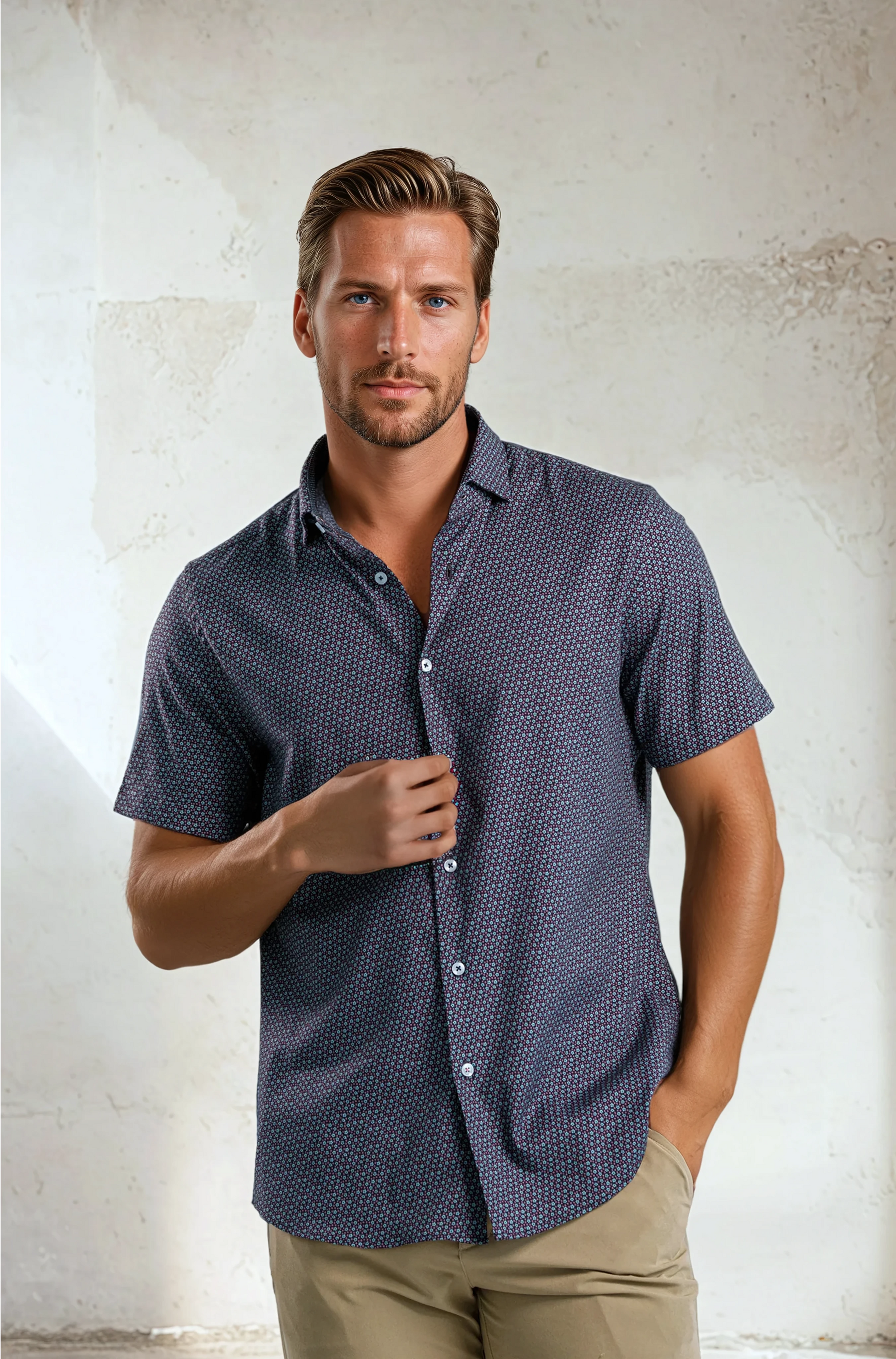 Man wearing a patterned blue shirt against a textured white wall