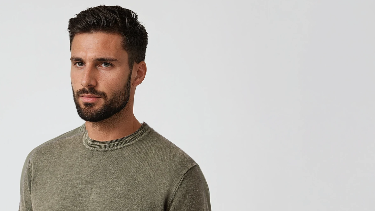 Man wearing an olive green t-shirt and black pants on a white background